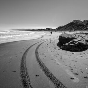 Person walking on beach with tire tracks